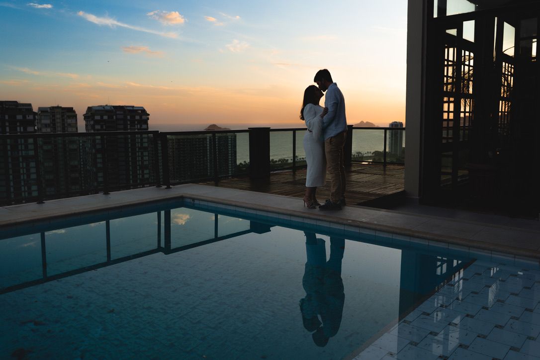 Silhueta de Maria Isabella e Eric junto à piscina ao pôr do sol